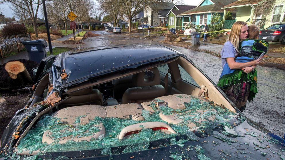 Anna Miller-Jessel and her son Kaydan Seai, 2, survey damage in their Eugene, Ore., Dec. 10, 2015, after a wind and rain storm moved through overnight, toppling several trees along the street and causing damage to cars and homes. 
