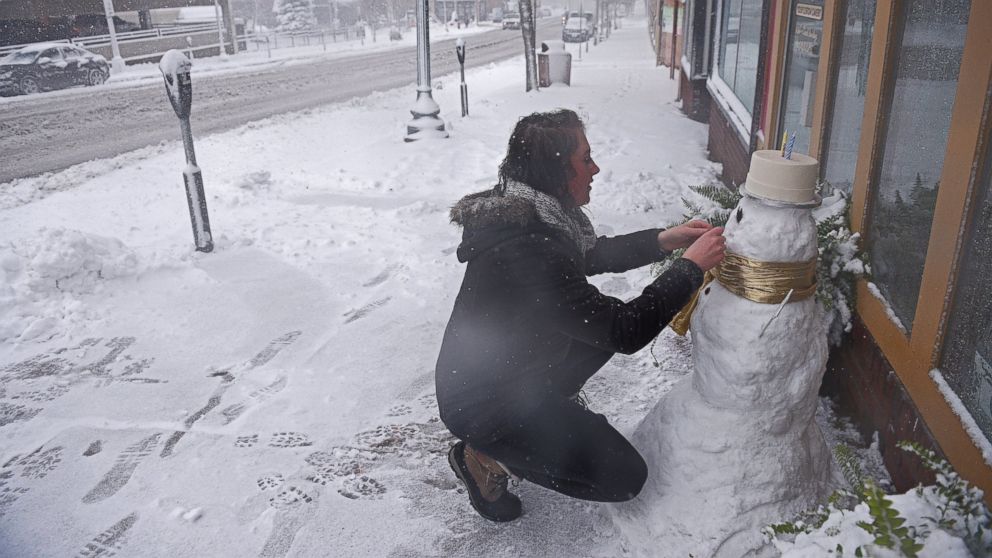 Cassie Maurer, with QT Cakes, puts the finishing touches on a snow man in front of the shop during a snow storm, Nov. 18, 2016, in Sioux Falls, South Dakota.