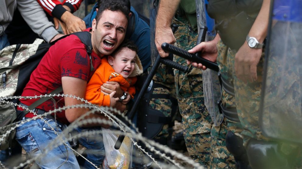 A refugee holding a boy react as they are stuck between Macedonian riot police officers and refugees during a clash near the border train station of Idomeni, northern Greece, Aug. 21, 2015. 