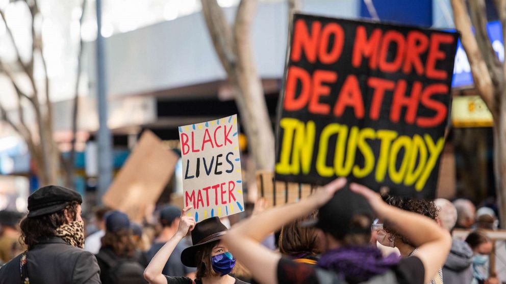 PHOTO: A protester holds a 'Black Lives Matter' and 'No more deaths in custody' placards during a demonstration in Brisbane, Australia, June 6, 2020.