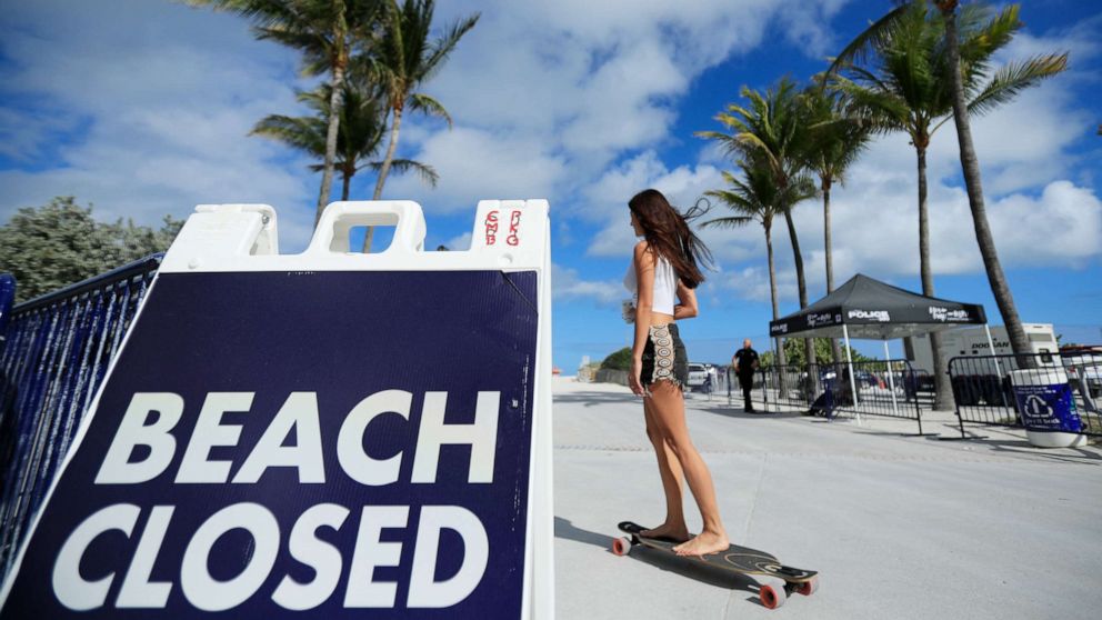 PHOTO: A skateboarder passes a "Beach Closed" sign on the boardwalk on March 22, 2020 in Miami Beach, Florida. The city of Miami Beach has closed all parks and beaches due to COVID-19, however the boardwalk is open for people to exercise.