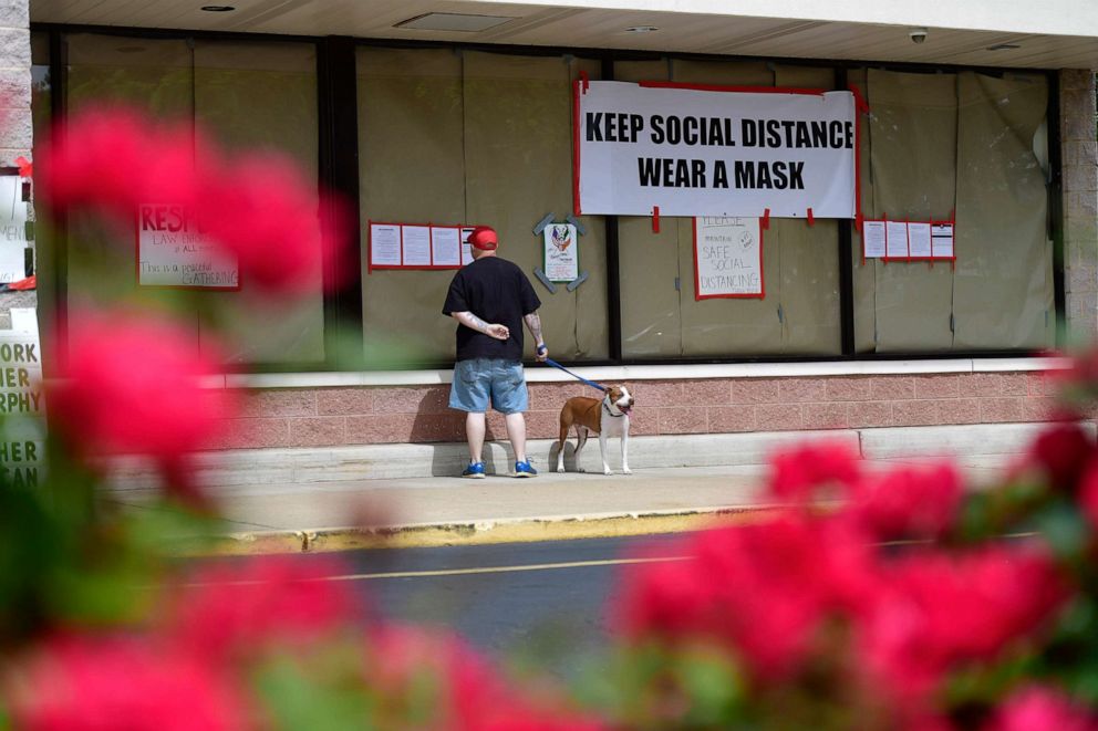 PHOTO: A man walking his dog reads notices outside of Atilis Gym below a placard stating "KEEP SOCIAL DISTANCE WEAR A MASK" on May 20, 2020 in Bellmawr, New Jersey.