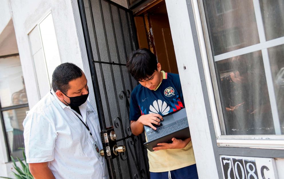 PHOTO: David Palencia from JFK helps Angel, 13, to connect his computer to the Wifi Hotspot provided by a parked van from JFK Transportation in order to follow his online classes, September 16, 2020, in Santa Ana, California. 