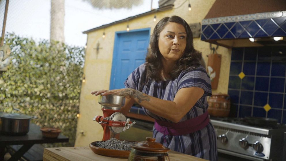 PHOTO: Claudia Serrato grinds corn in a mill as she prepares atole, a warm, sweet drink that has existed for millennia. She says preparing food from scratch engages us with the food, and by extension, our heritage. 