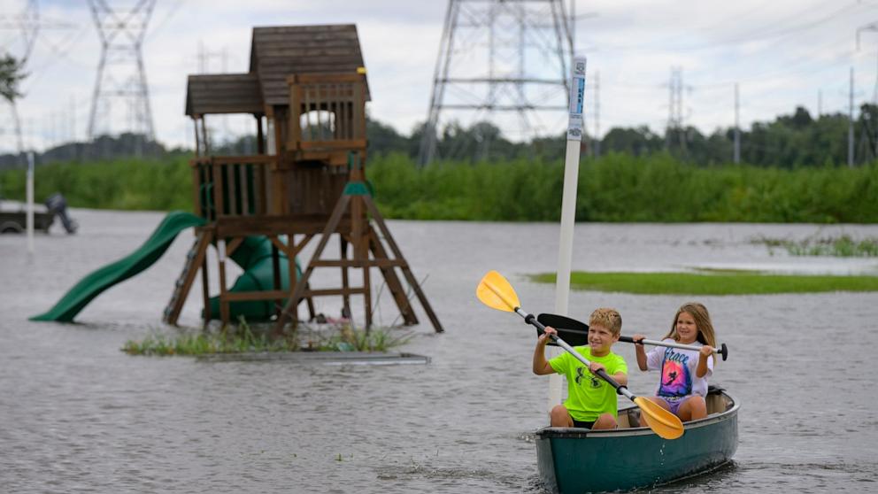 PHOTO: Siblings Avery, 10, and Grace LeBlanc, 7, canoe in their backyard next to playground equipment after flooding from Hurricane Francine in Montz, La., in St. Charles Parish, Sept. 12, 2024.