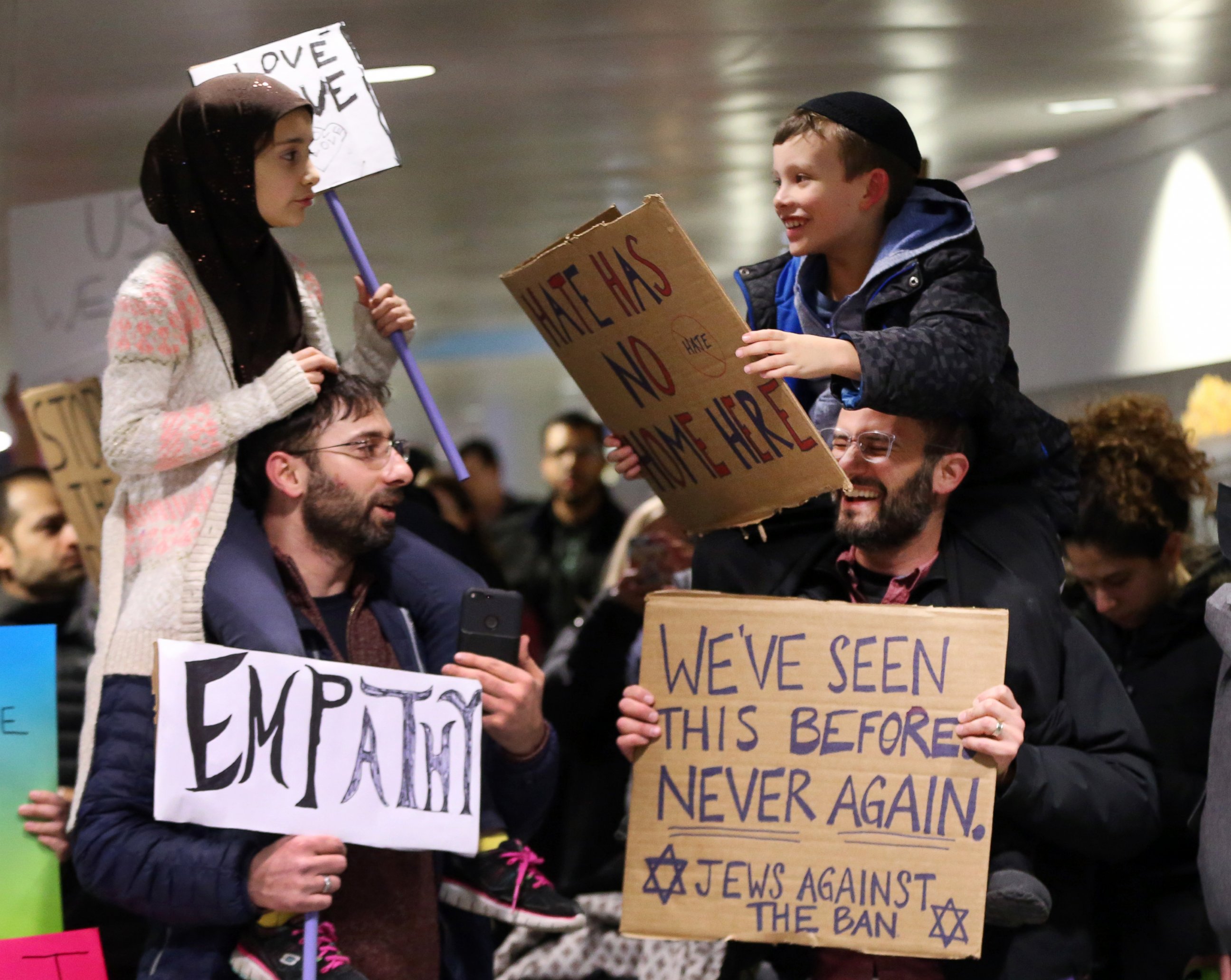 PHOTO: Meryem Yildirim, 7, left, sits on her father, Satih, of Schaumburg, and Adin Bendat-Appell, 9, right, sits on his father, Rabbi Jordan Bendat-Appell, of Deerfield, during a protest, on Jan. 30, 2017 at O'Hare International Airport in Chicago.