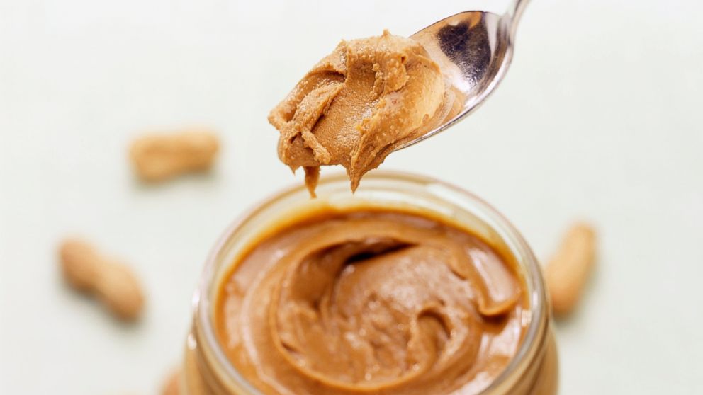 PHOTO: A spoonful of natural peanut butter from a jar with peanuts in the background.