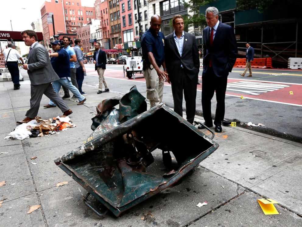 PHOTO: New York Mayor Bill de Blasio (R) and New York Governor Andrew Cuomo (C) stand in front of a mangled dumpster while touring the site of an explosion that occurred, on Sept. 18, 2016, in the Chelsea neighborhood of New York City. 