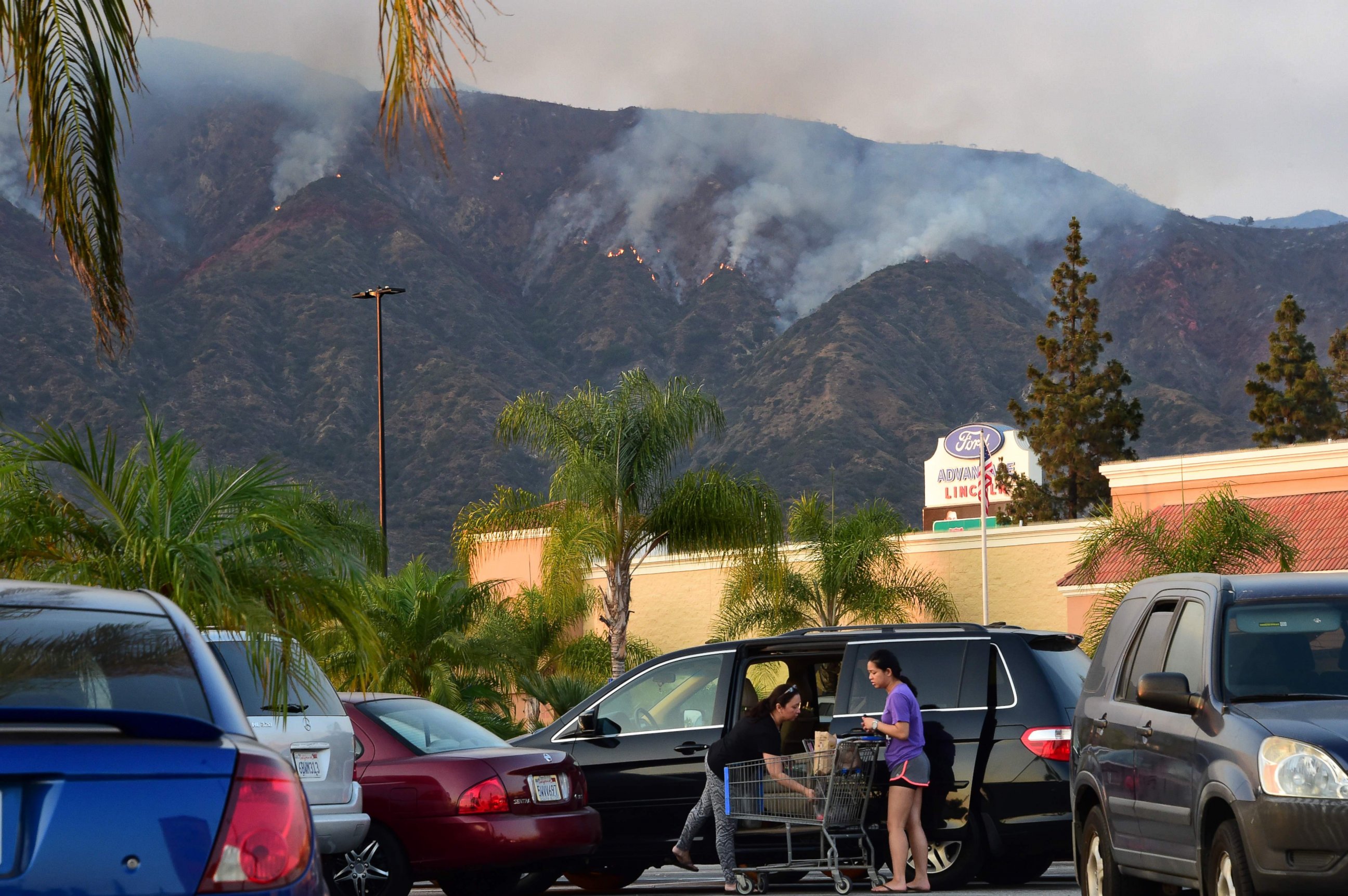 PHOTO: Shoppers load their car with the purchases against the backdrop of the smoke from the San Gabriel Complex Fire in the Angeles National Forest, near Duarte, Calif., on June 21, 2016.