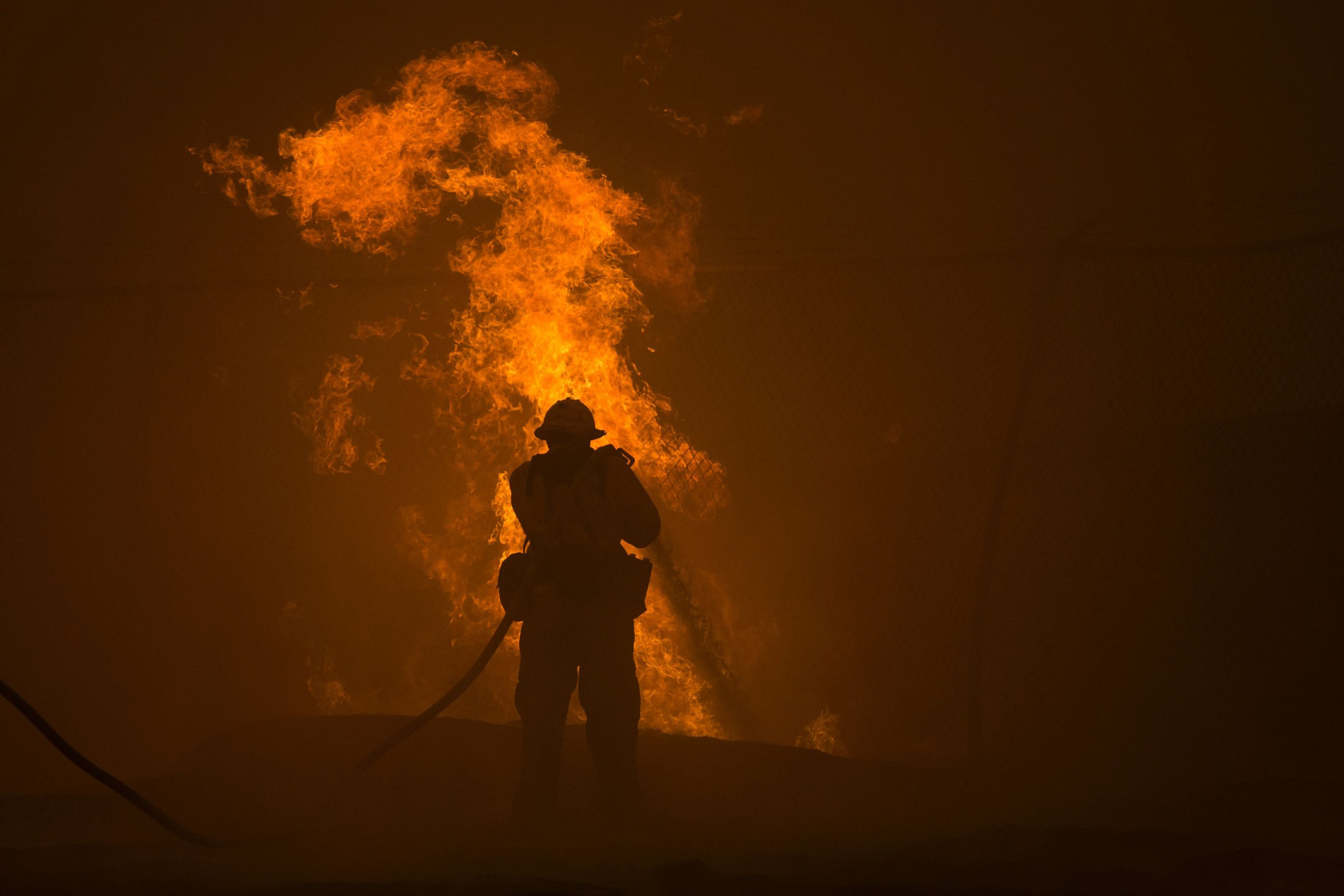PHOTO: A firefighter hoses down burning pipes near a water tank at the Sand Fire, July 23 2016 near Santa Clarita, California.
