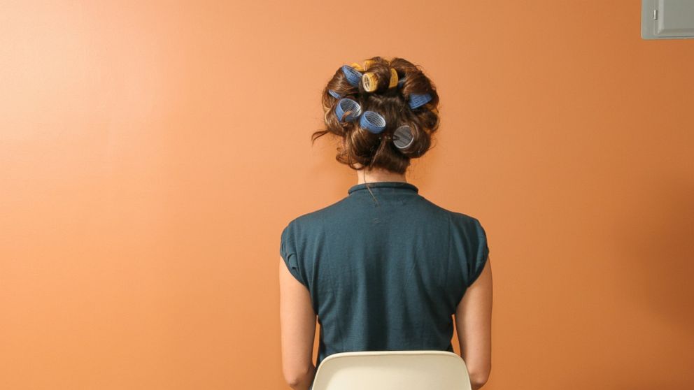 PHOTO: A woman sits wearing curlers in her hair.