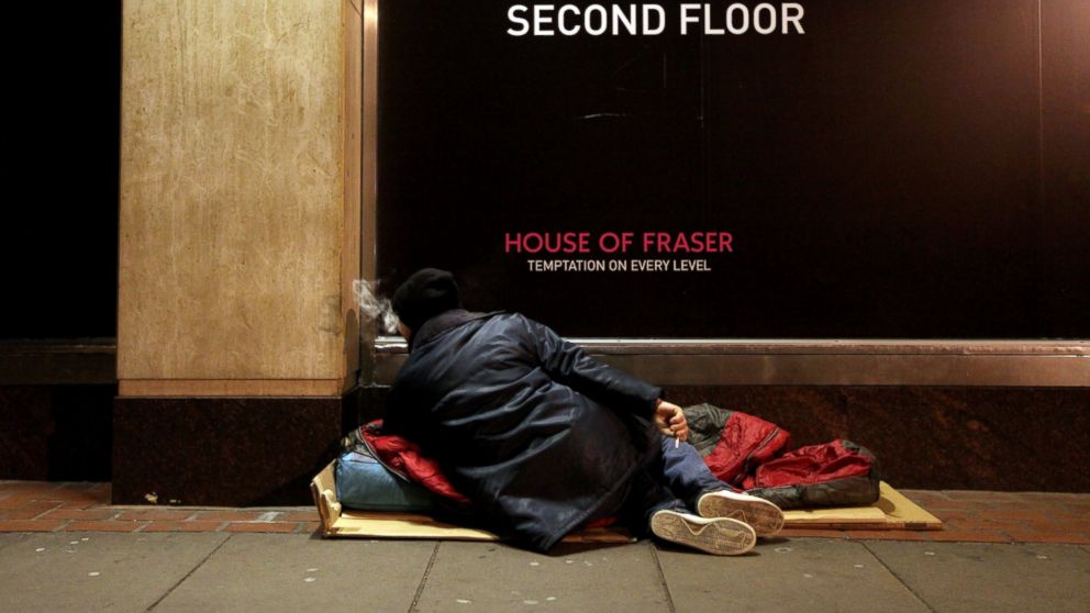 PHOTO: A homeless man rests on his sleeping bag in the street next to a department store.