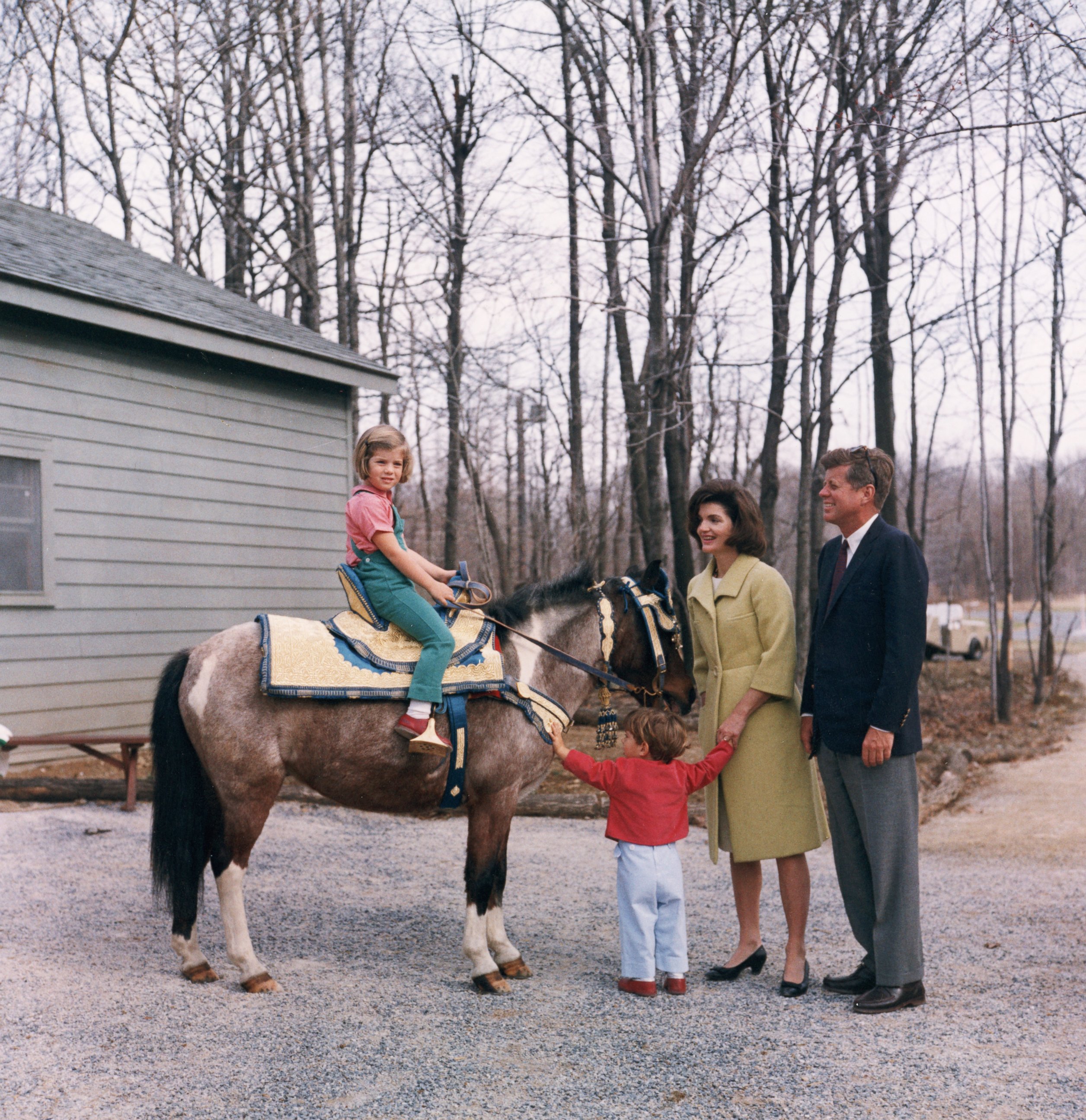 PHOTO: US President John F Kennedy stands with his wife, First Lady Jacqueline Bouvier Kennedy, as their daughter, Caroline, sits atop a pony and their son, John Jr. holds his arms out, March 31, 1963.
