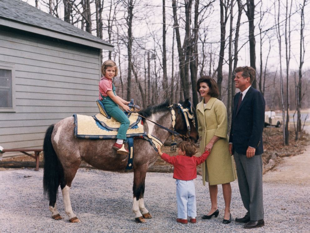 PHOTO: US President John F Kennedy stands with his wife, First Lady Jacqueline Bouvier Kennedy, as their daughter, Caroline, sits atop a pony and their son, John Jr. holds his arms out, March 31, 1963.