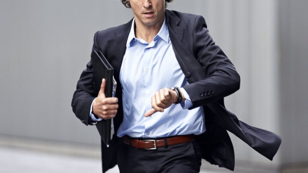 A businessman is pictured checking his wristwatch while rushing in this stock image. 
