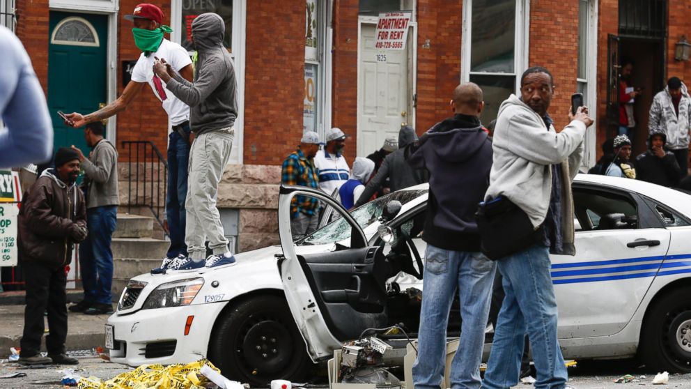 PHOTO: People stand on a damaged Baltimore police car near the intersection of Pennsylvania Avenue and North Avenue on April 27, 2015 in Baltimore, Md.