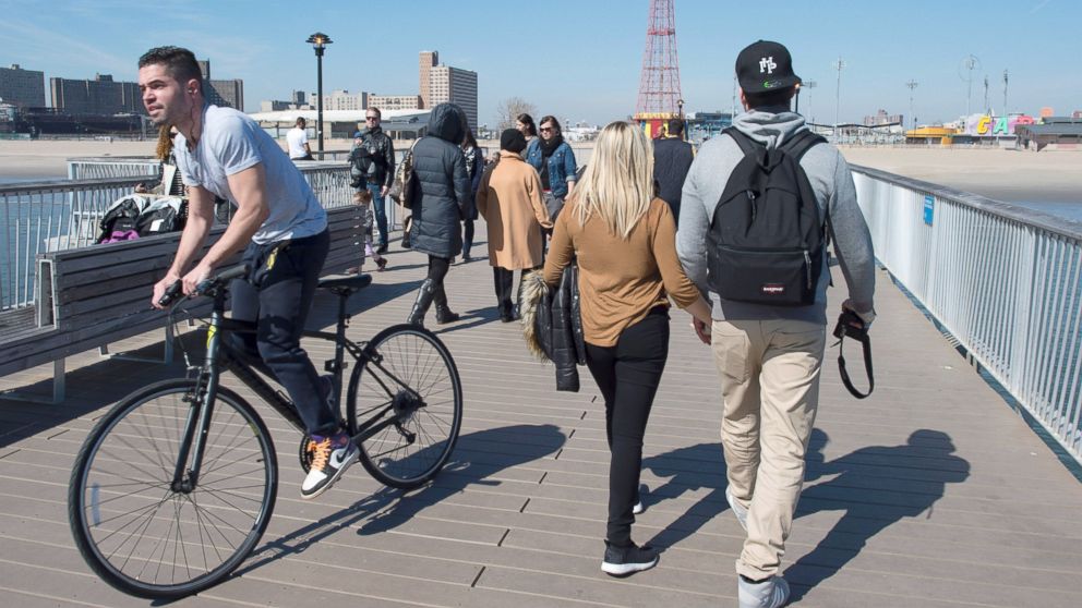 People walk past a biker on the pier at Coney Island on March 9, 2016 in New York