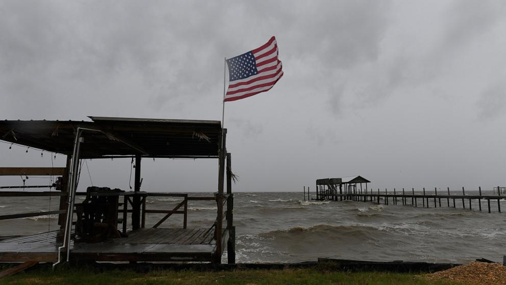 PHOTO: An American flag flaps in the wind generated by the effects of Isaias on an empty beach on Friday, Oct. 9, loom overhead, Oct. 9, 2026, in Mon Louis Island, Ala.