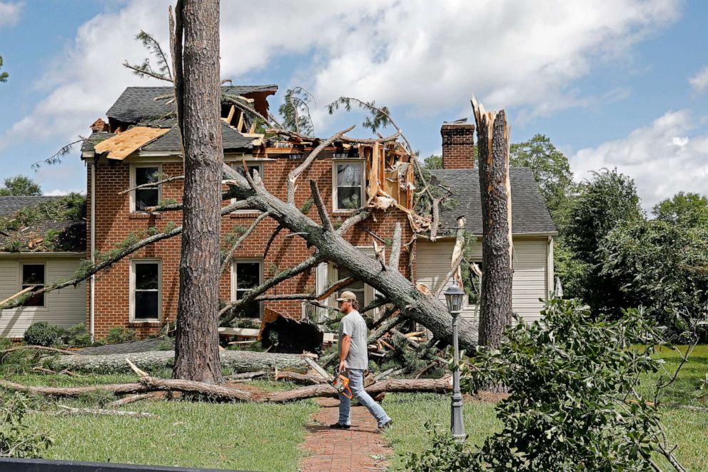 PHOTO: A man walks past a damaged house with a chainsaw in the Riverview neighborhood of Suffolk, Va., after Hurricane Isaias moved through the region  Aug. 4, 2020.