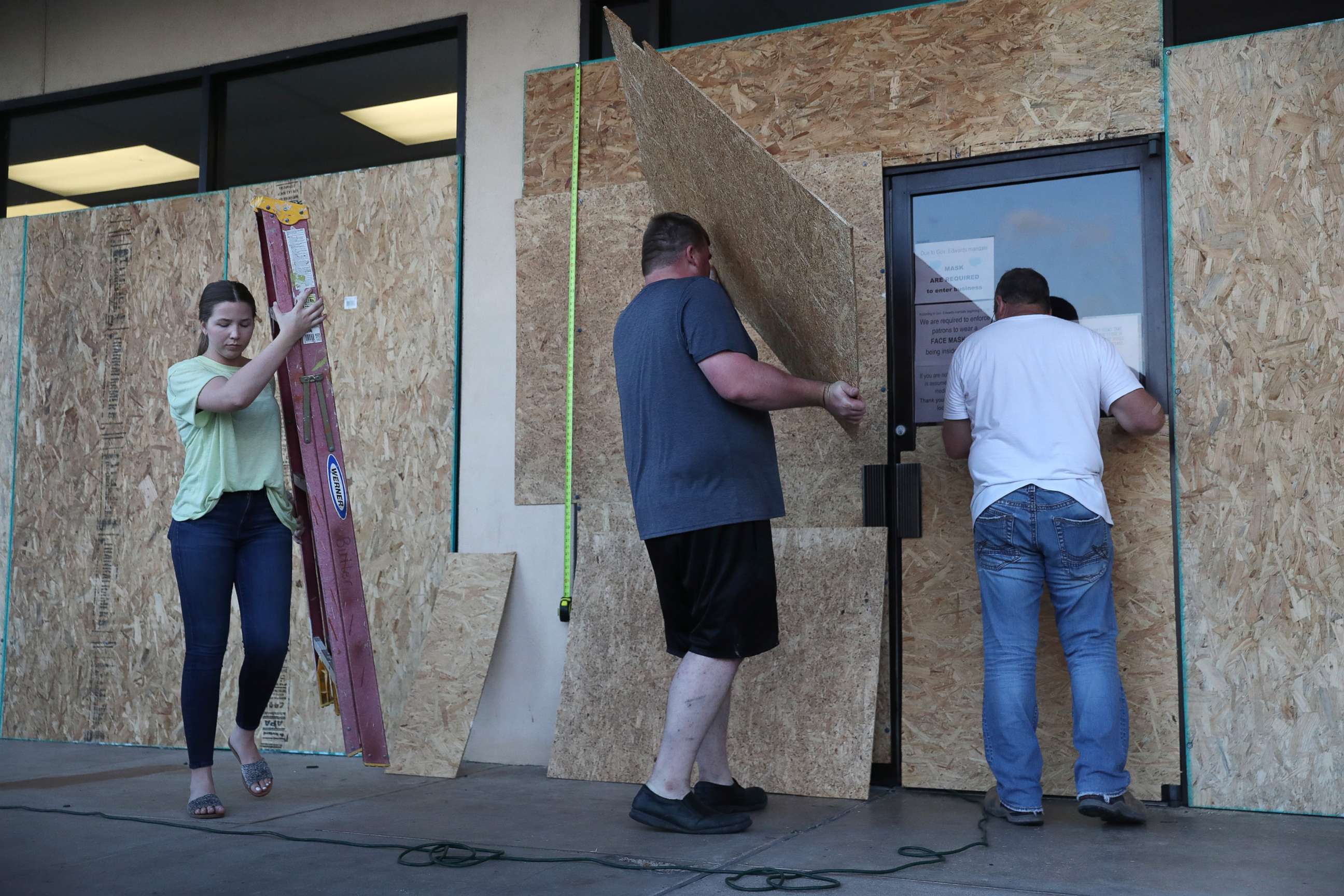 PHOTO: LAKE CHARLES, LOUISIANA- AUGUST 25:   (L-R) Lacey Buller, Tyler Arnold and Mike Buller work on placing plywood over the windows of their business before the arrival of Hurricane Laura on August 25, 2020 in Lake Charles, Louisiana. 