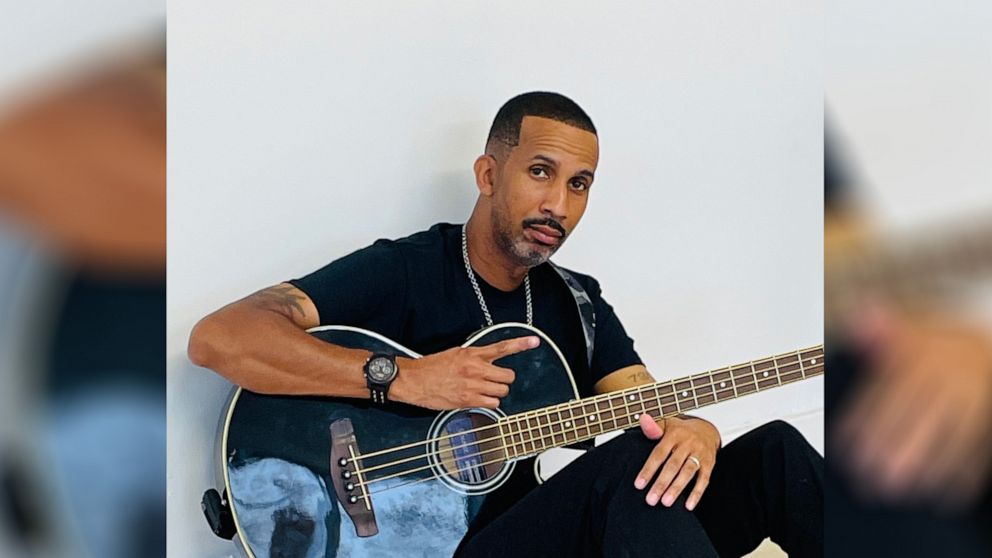 PHOTO: McKinley "Mac" Phipps, Jr. is pictured posing with an acoustic bass guitar.