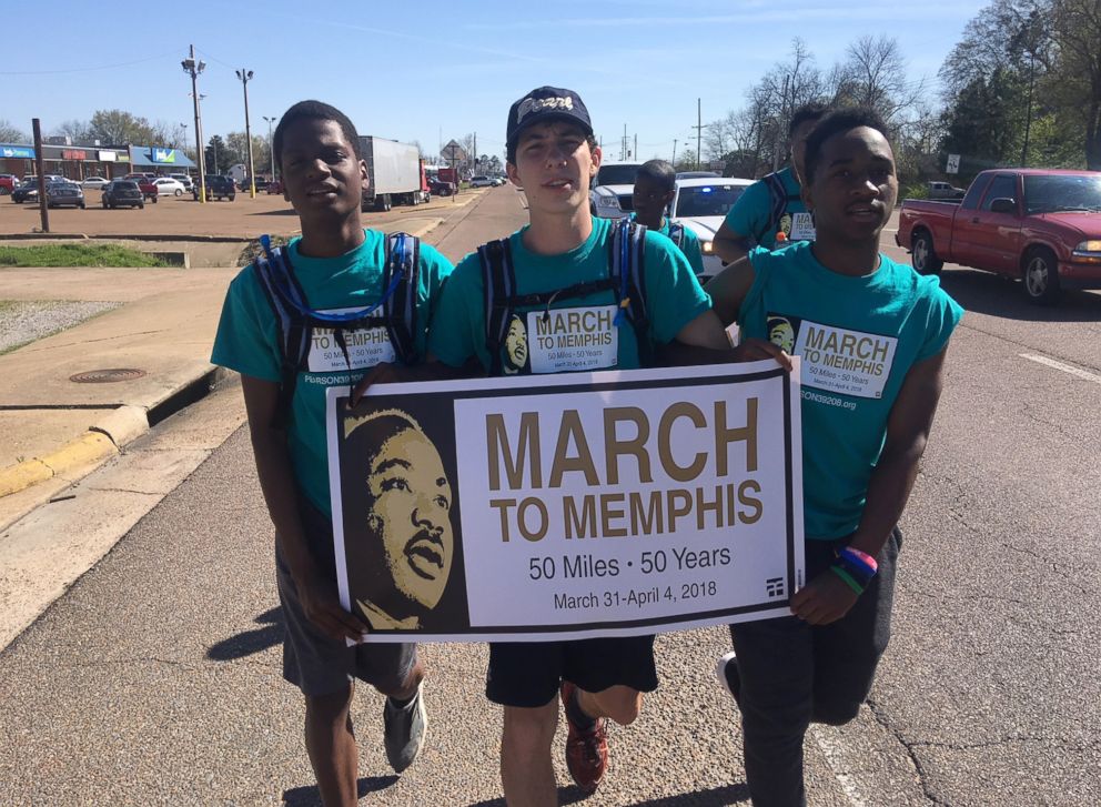 PHOTO: Three march participants, linking arms in solidarity and carrying the "March to Memphis" banner, head down Highway 61 in Dundee, Miss., March 31, 2018.