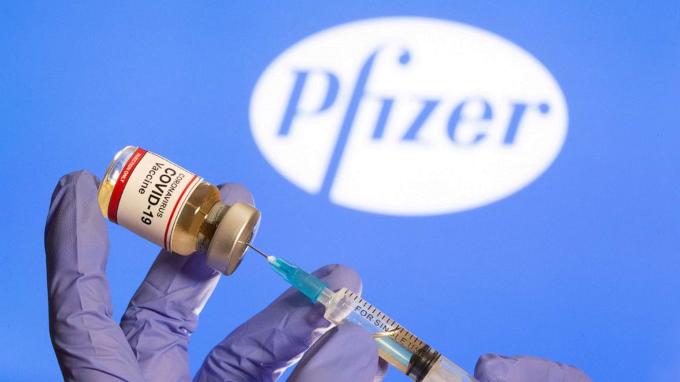 FILE PHOTO: A woman holds a small bottle labeled with a "Coronavirus COVID-19 Vaccine" sticker and a medical syringe in front of displayed Pfizer logo in this illustration taken, October 30, 2020. 
