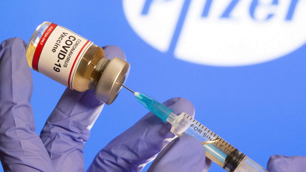FILE PHOTO: A woman holds a small bottle labeled with a "Coronavirus COVID-19 Vaccine" sticker and a medical syringe in front of displayed Pfizer logo in this illustration taken, October 30, 2020. 