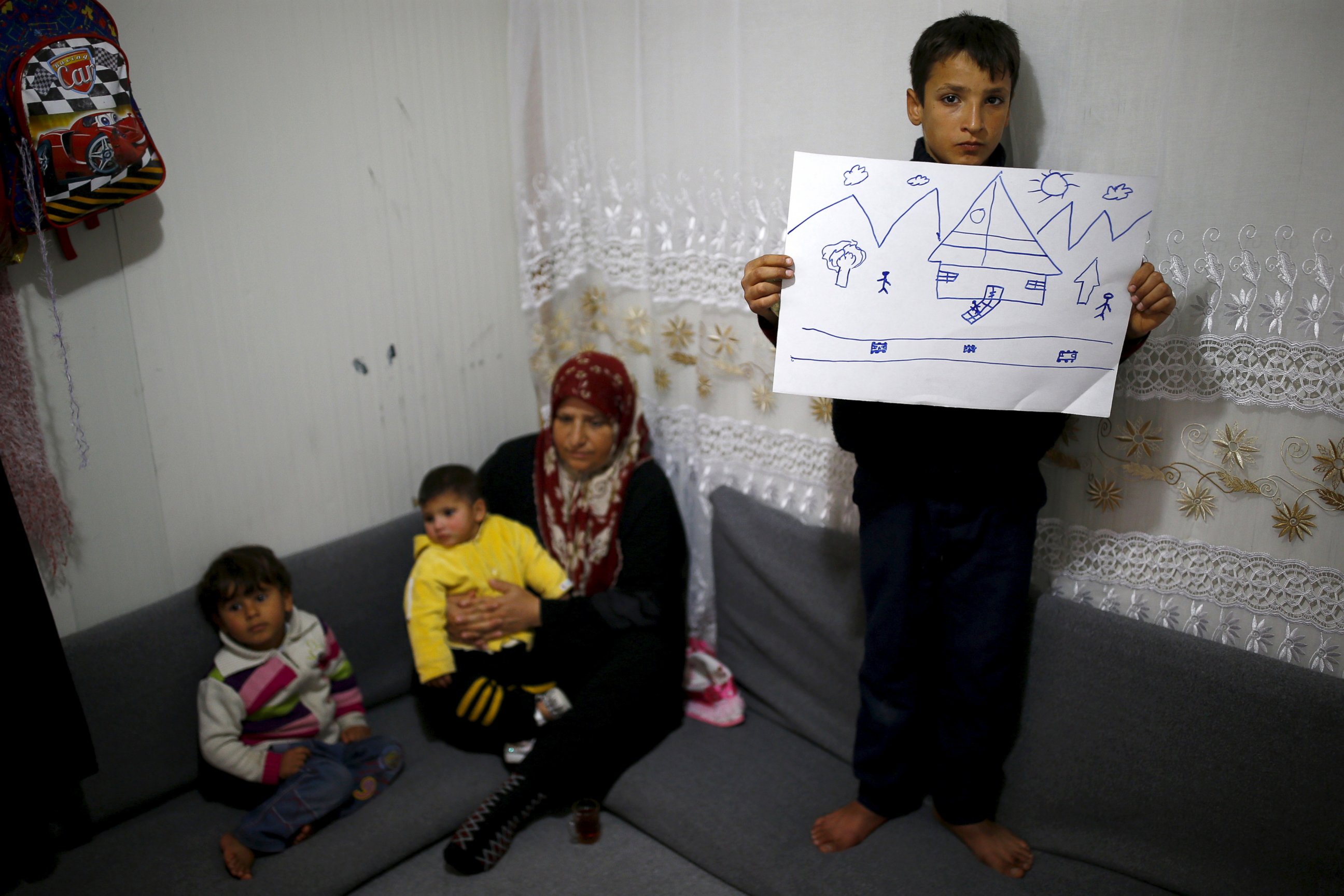 PHOTO: Syrian refugee Ahmet Cemal, 12, shows a drawing of home as his mother and his two brothers sit next to him in their tent in Nizip refugee camp in Gaziantep province, Turkey, Dec. 13, 2015. 
