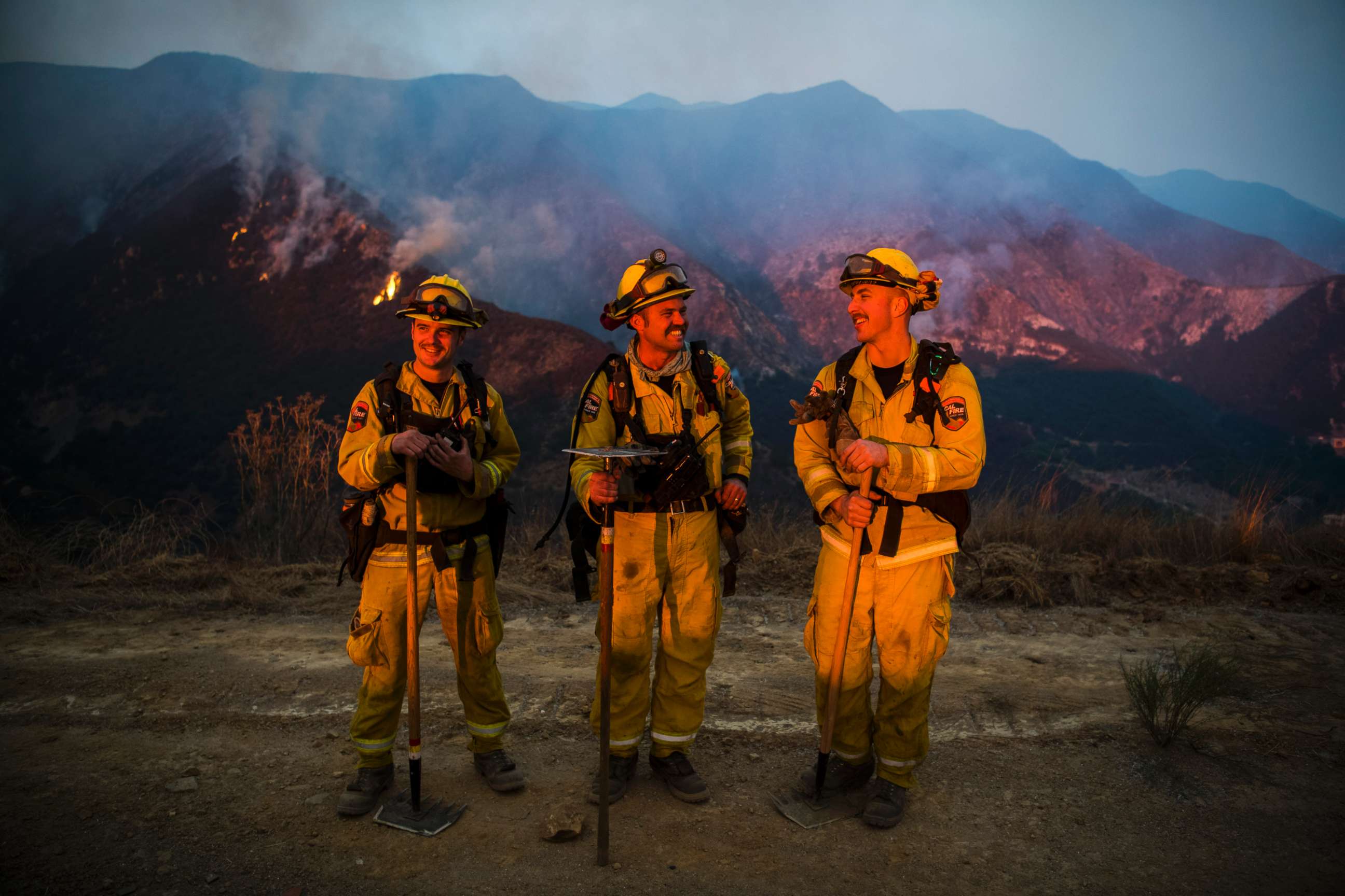 PHOTO: Firefighters Jesse Prins, Clinton Frazell, and Jesse Cole from a Cal Fire strike team dispatched from Lake County, Calif., take a moment to observe the last air tanker drops of the day during sunset on Dec. 11, 2017.  