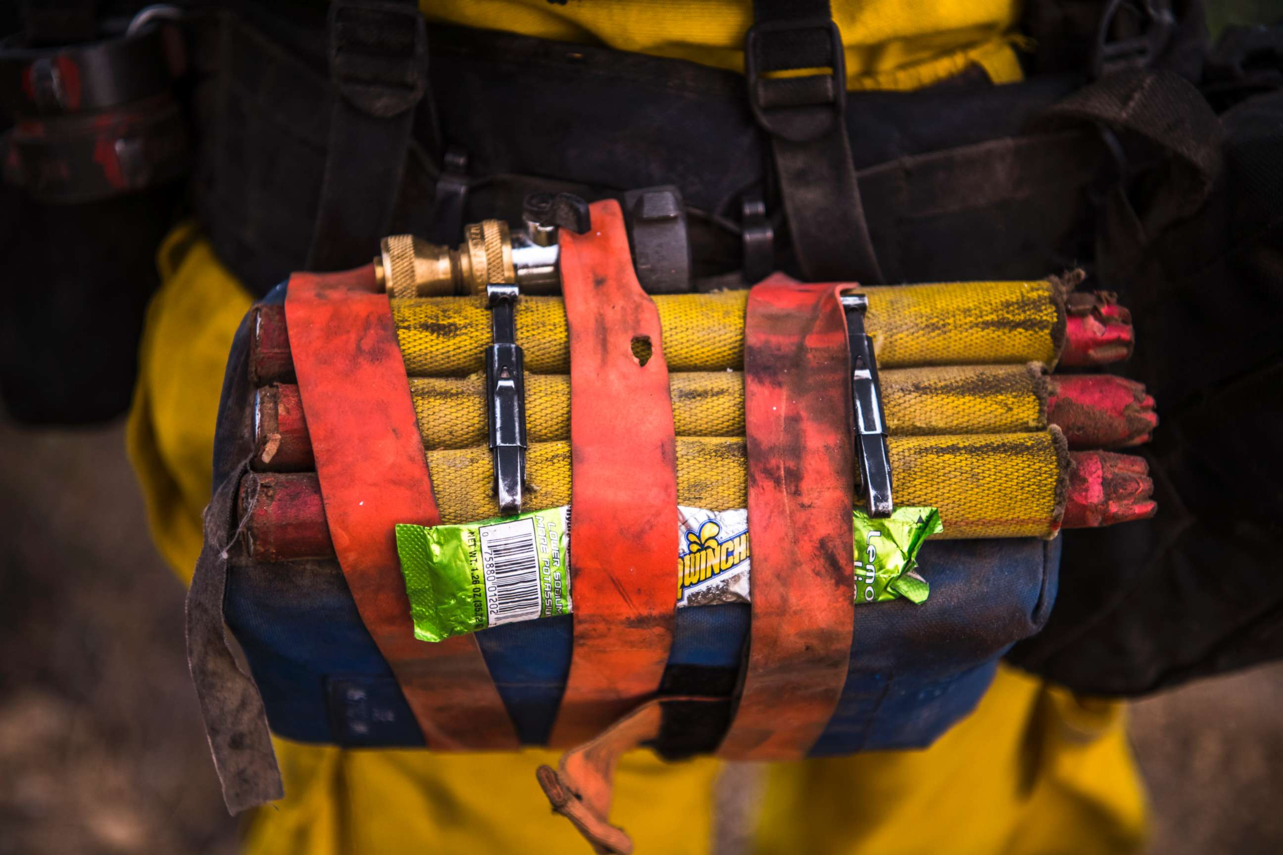 PHOTO: A Cal Fire wildland firefighter carries a fire shelter, fusees, hose nozzle, and powdered sports drink mix in their web gear. 