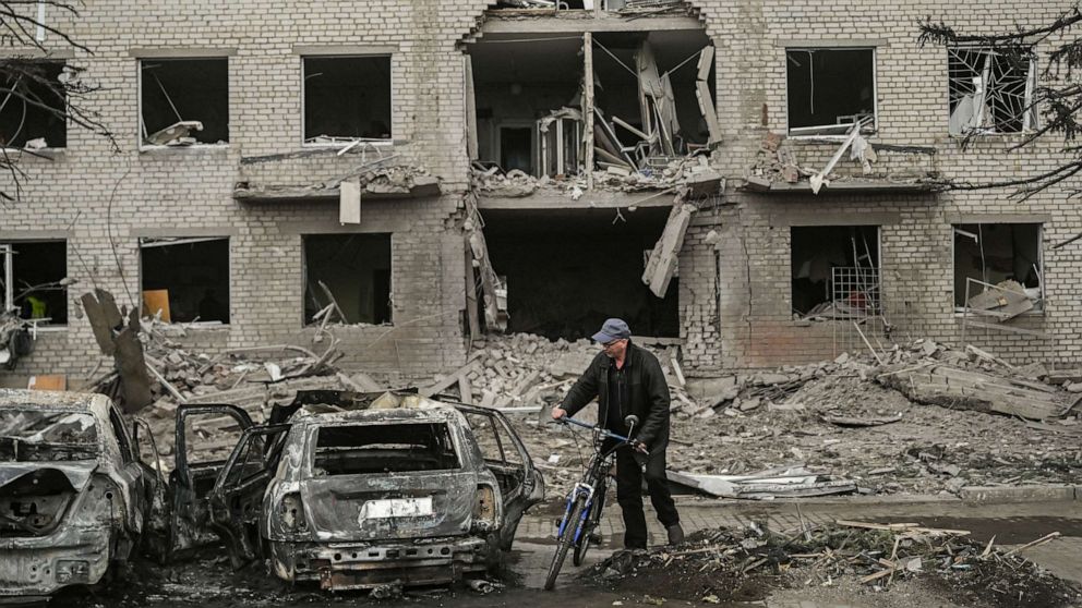 PHOTO: A man with his push bike stops to look at the remains of a destroyed vehicle in front of a destroyed building after a deadly strike in the city of Sloviansk, Ukraine, March 27, 2023.