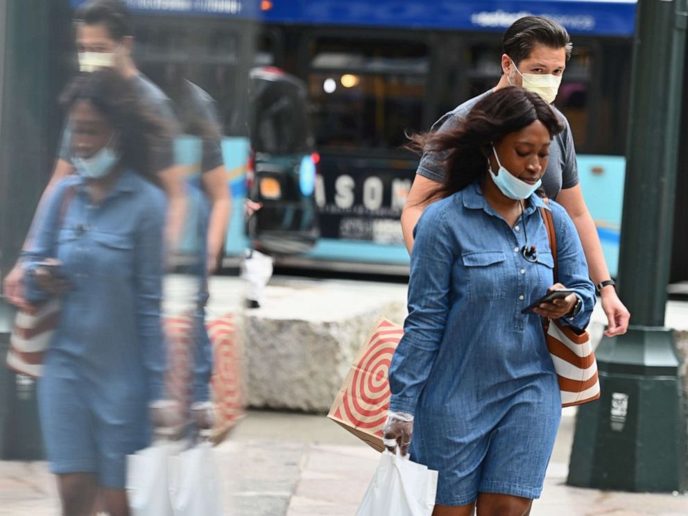 PHOTO: (FILES) In this file photo people wearing facemasks carry shopping bags as they walk on a street near Herald Square on June 25, 2020 in New York City.