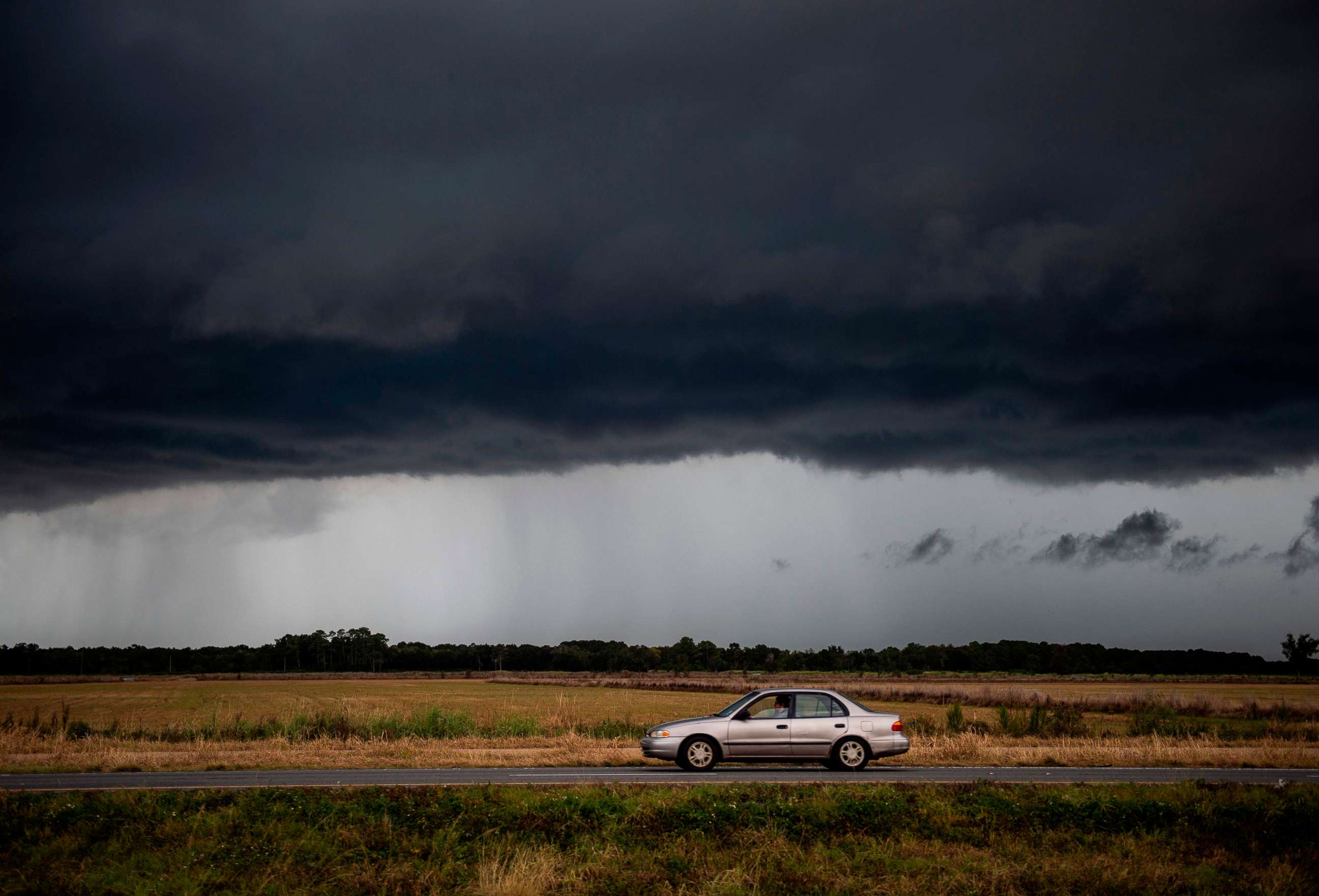 PHOTO: A car drives under an ominous rain cloud from tropical storm Marco as locals prepare for the arrival of hurricane Laura near Lake Charles, Louisiana on August 25, 2020. 