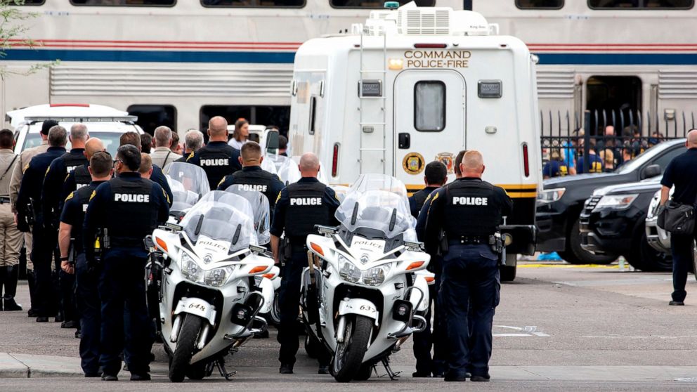 Tucson Police officers and other law enforcement officers stand at attention as the body of a Drug Enforcement Administration special agent is removed from an Amtrak train and loaded into a van from the Pima County Medical Examiner following a shooti
