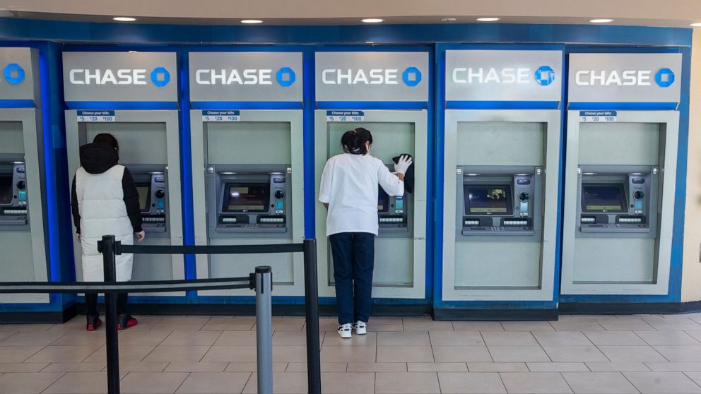 A Chase bank employee, right, disinfects the branches ATMs to fend off coronavirus as a customer uses another along Main St., Tuesday, March 24, 2020, in the Flushing neighborhood of Queens borough of New York. (AP Photo/Mary Altaffer)