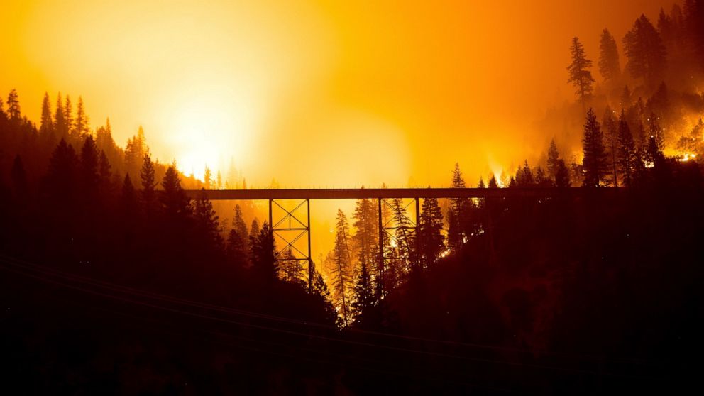 Seen in a long exposure photograph, the Dixie Fire burns behind a bridge in Plumas County, Calif., on Sunday, July 25, 2021. (AP Photo/Noah Berger)