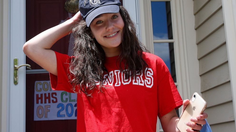 In this June 1, 2020 photo, high school graduate Lizzie Quinlivan wears a Georgetown University cap at her home in Hingham, Mass. Quinlivan has opted to attend closer-to-home Georgetown instead of colleges on the west coast which were on her original