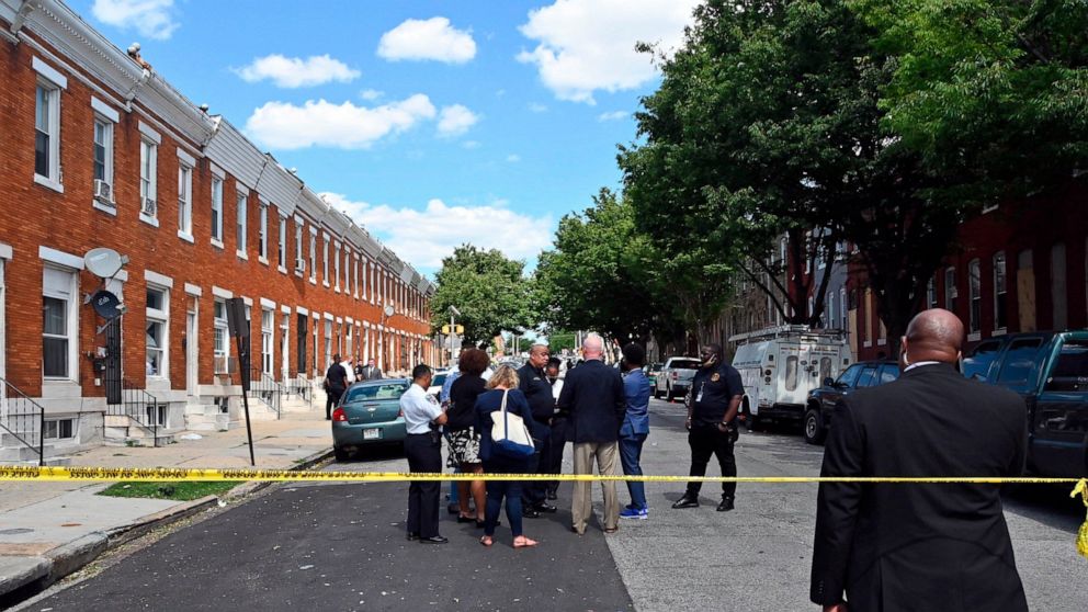 Baltimore Police Commissioner Michael Harrison, center, Baltimore Mayor Brandon Scott, second from right, confer at the scene of a shooting, Wednesday, June 16, 2021, in Baltimore. One person was killed and five others were wounded Wednesday when gun