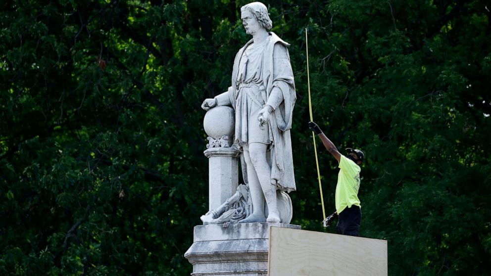 FILE - In this June 16, 2020 file photo, a city worker measures the statue of Christopher Columbus at Marconi Plaza in Philadelphia. The statue remains hidden by a plywood box while its fate is decided in the courts, but the box has now been painted 