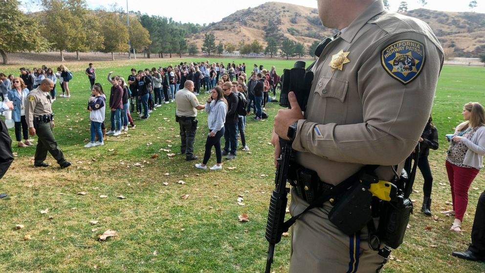 A police officer stands guard as students wait to be reunited with their parents following a shooting at Saugus High School that injured several people, Thursday, Nov. 14, 2019, in Santa Clarita, Calif. (AP Photo/Ringo H.W. Chiu)