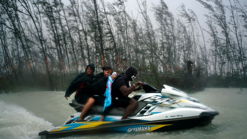 A woman who was trapped by flood waters caused by Hurricane Dorian is taken to safety after she was rescued by volunteers on a jet ski near the Causarina bridge in Freeport, Bahamas, Tuesday, Sept. 3, 2019. The storm's punishing winds and muddy brown