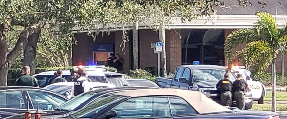 Law enforcement officials take cover outside a SunTrust Bank branch, Wednesday, Jan. 23, 2019, in Sebring, Fla. Authorities say theyve arrested a man who fired shots inside the Florida bank. (The News Sun via AP)