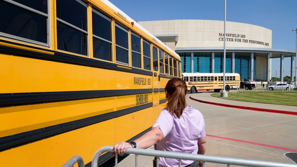 School busses depart past a law enforcement official after dropping off Timberview High School children at the Mansfield ISD Center For The Performing Arts, Wednesday, Oct. 6, 2021 in Mansfield, Texas, following a school shooting at Timberview in nea
