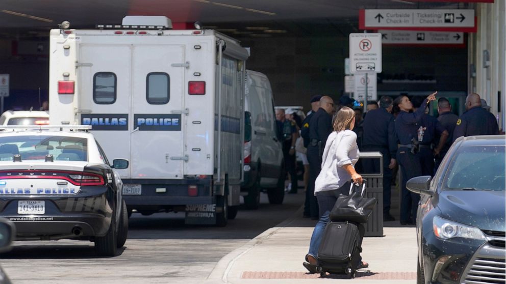 A traveler makes her way past emergency responders standing outside the ticketing and check in area at Dallas Love Field in Dallas, Monday, July 25, 2022. A 37-year-old woman fired several gunshots, apparently at the ceiling, inside of Dallas' Love F