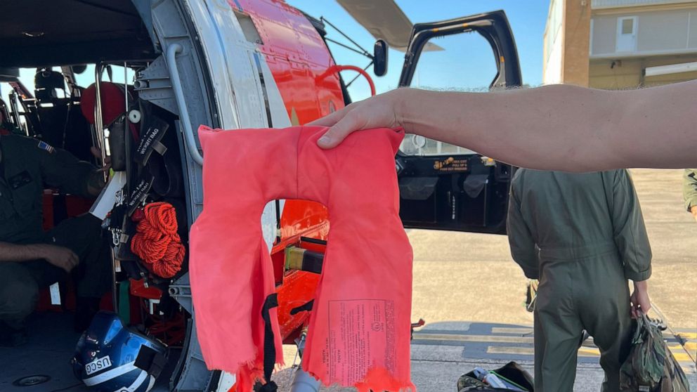 In this image provided by the U.S. Coast Guard, a Coast Guard Air Station New Orleans aircrew member holds up a torn life jacket from a recent rescue off the coast of Empire, La., on Oct. 9, 2022. Three men whose fishing boat sank in the Gulf of Mexi