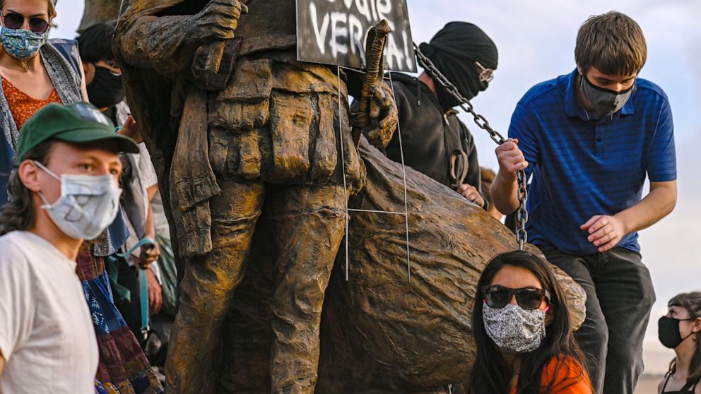 Protesters attach a chain to a statue of Spanish conquerer Juan de Oñate in Albuquerque, N.M., Monday, June 15, 2020. One man was shot during an exchange between protesters and armed members of the New Mexico Civil Guard, a civilian group trying to p