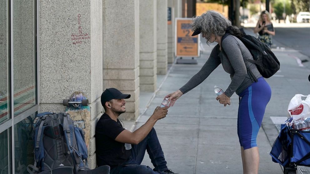 Freddie Ramirez, left, is handed a bottle of water from Kim Burrell, in Sacramento, Calif., Tuesday, Sept. 6, 2022. Burrell and Debbie Chang, unseen, passed out water and snacks to those they find in need on the streets. Temperatures in the Sacrament