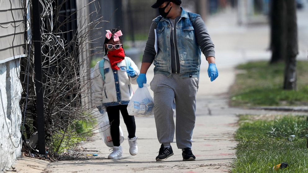 In this April 7, 2020, photo, Erica Harris, right, and her daughter Jordan, wear their protective masks as they walk back home after getting a lunch and homework from the child’s school on Chicago’s Southside in Chicago. As the coronavirus tightened 
