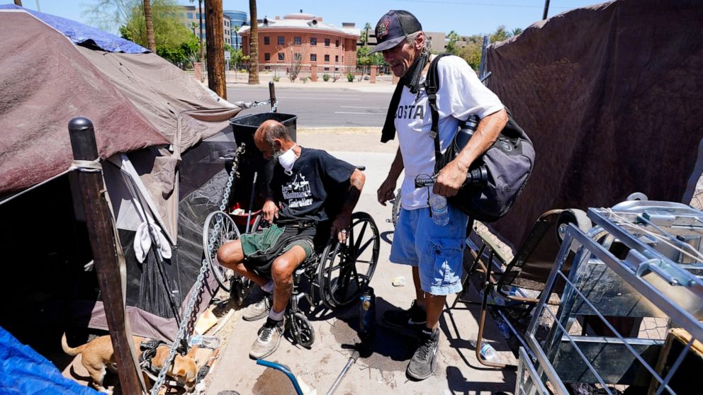 "Cueball", left, talks about his dog Lindsay with neighbor Terry Reed, right, at their tents Friday, May 20, 2022, in Phoenix. Hundreds of homeless people die in the streets each year from the heat, in cities around the U.S. and the world. The ranks 